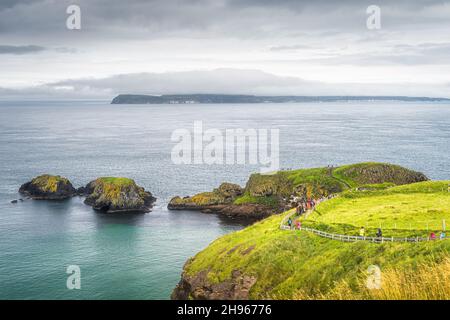 Groupe de personnes sur le sentier menant à Carrick un pont de corde Rede avec une vue sur l'île de Rathlin, Ballycastle, Wild Atlantic Way, Irlande du Nord Banque D'Images