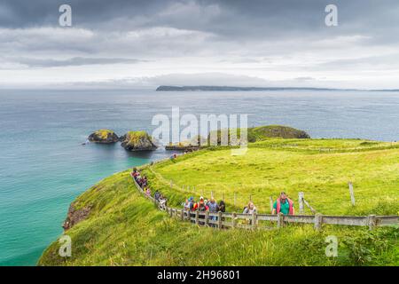 Ballycastle, août 2019 Groupe de personnes sur le sentier menant à Carrick un pont de corde Rede avec vue sur l'île de Rathlin, Wild Atlantic Way, Irlande du Nord Banque D'Images