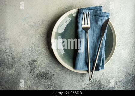 Assiettes en céramique, couverts de même couleur avec serviette striée servis sur fond de béton gris Banque D'Images