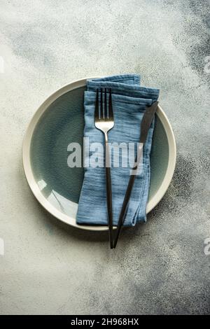 Assiettes en céramique, couverts de même couleur avec serviette striée servis sur fond de béton gris Banque D'Images