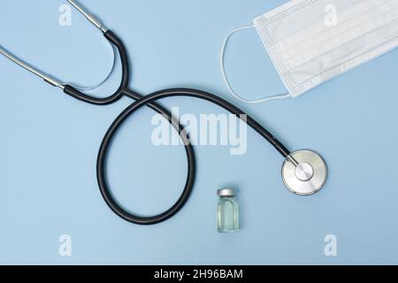 Flacon avec médicament médical, masque facial et stéthoscope.Flacons de vaccin coronavirus COVID-19, seringue et stéthoscope sur fond bleu.Vaccination Banque D'Images