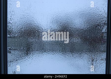 Vue à travers une fenêtre recouverte d'une couche de glace.Gouttes de pluie figées dans le volet de la fenêtre. Banque D'Images