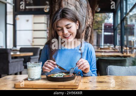 Une jeune femme dans un café dines sur le shakshuka traditionnel et ayran. Banque D'Images