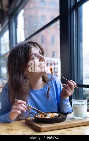 Une jeune femme dans un café dines sur le shakshuka traditionnel et ayran. Banque D'Images