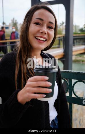 Une jeune femme souriante boit du café à l'extérieur Banque D'Images