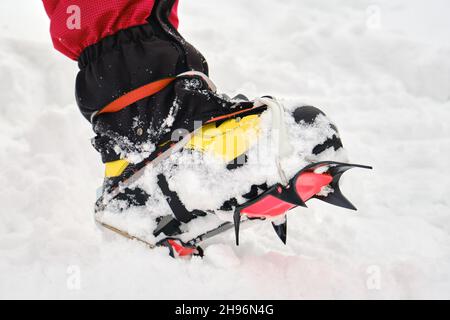 Gros plan des crampons d'alpinisme avec des dents nettes visibles sur un pied avec des guêtres, sur la neige.Randonnée d'hiver, équipement, équipement. Banque D'Images