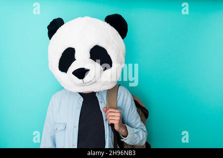 Jeune homme en masque panda tenant un sac à dos sur fond coloré Banque D'Images