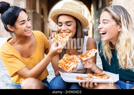 Trois gaies multiraciales femmes de manger de la pizza dans la rue Banque D'Images