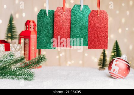 Quatre étiquettes cadeau ou étiquettes avec espace pour le texte sur la composition festive de Noël avec branche de sapin, décor de boule rouge, lanterne sur la neige contre un Banque D'Images