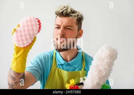 Beau jeune homme avec des fournitures de nettoyage près du mur de lumière Banque D'Images