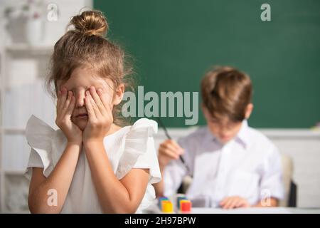 Une fille de l'école intelligente pleurer.Une écolière en uniforme couvrant son visage avec son bras pleure triste d'intimidation à l'école debout devant le tableau noir Banque D'Images