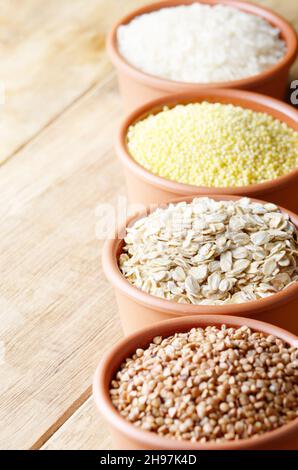 Grains de céréales placés dans des bols en céramique sur une table en bois Banque D'Images