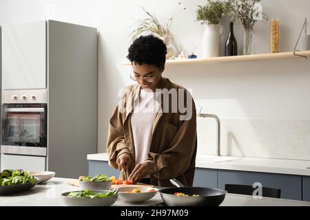 Bonne jeune femme afro-américaine préparant des aliments dans la cuisine. Banque D'Images