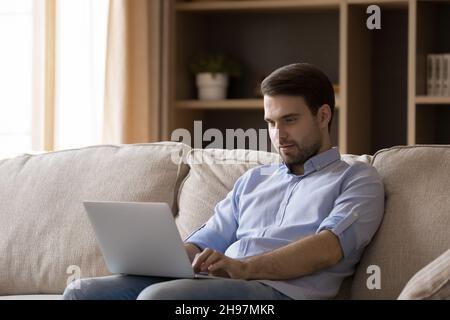 Jeune homme d'affaires souriant et concentré travaillant à domicile sur un ordinateur portable Banque D'Images