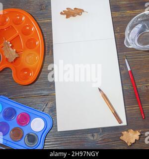 Carnet d'esquisses, peintures à l'aquarelle, palette et feuilles d'automne sèches sur table rustique sombre.Concept scolaire.Copier l'espace Banque D'Images