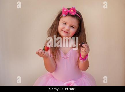 Portrait d'un enfant dans une robe de ballet.Fille posant, tenant un morceau de chocolat et une fraise dans ses mains, souriant Banque D'Images