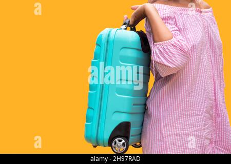 Valise de voyage en plastique turquoise. Fille en robe rose porte un sac sur fond jaune orange. En voyage Banque D'Images