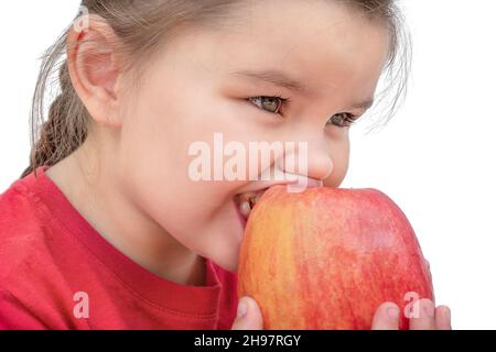 Un enfant dans un t-shirt rouge mord une pomme isolée sur fond blanc Banque D'Images