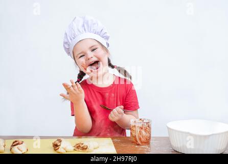 L'enfant dans le chapeau de chef mange une garniture pour la cuisson Banque D'Images