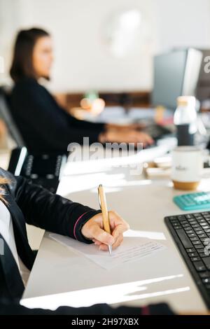 Gros plan des mains de la femme écrivant avec un stylo sur un bureau désordonné dans un bureau Banque D'Images