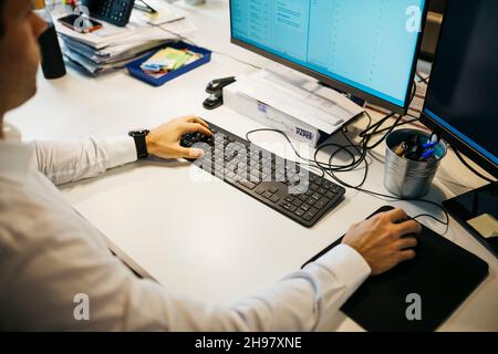 Gros plan des mains de l'homme tapant un ordinateur sur un bureau désordonné Banque D'Images