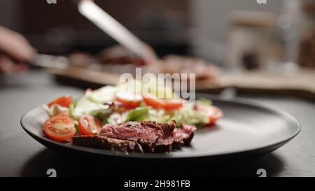 déposez les tranches de steak de new york sur une assiette noire avec des légumes verts et des tomates cerises mélangés, photo large Banque D'Images