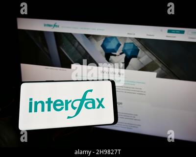 Personne tenant un téléphone portable avec le logo de l'agence de presse russe Interfax à l'écran en face de la page web de l'entreprise.Mise au point sur l'affichage du téléphone. Banque D'Images