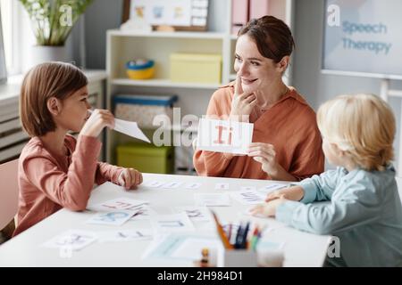 Jeune femme assise à la table avec des enfants montrant la carte avec la lettre et leur enseignant à lire Banque D'Images