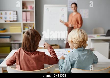 Vue arrière des enfants de l'école assis au bureau et étudiant pendant la leçon avec un enseignant dans la salle de classe Banque D'Images