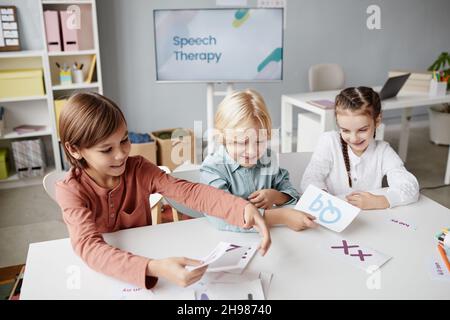 Groupe d'enfants de l'école faisant des mots à partir de cartes avec des lettres anglaises ensemble à la table pendant une leçon Banque D'Images