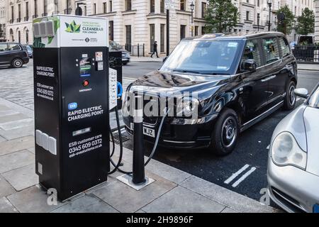 Une cabine électrique noire TX (fabriquée par LEVC) se recharge à un point de charge électrique rapide à St James's Square, Londres SW1, Royaume-Uni Banque D'Images