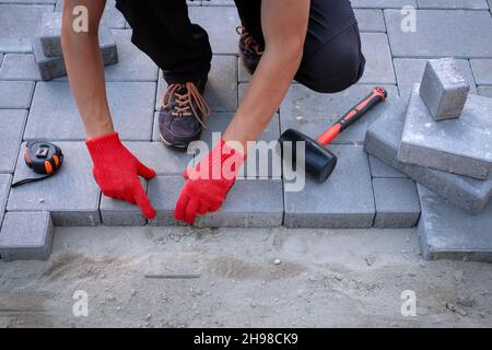 Le master en gants jaunes jette des pavés en couches. Brique de jardin pavage pavé la voie professionnelle par travailleur. La pose des dalles de béton gris dans la chambre cour sur la base de la fondation de sable. Banque D'Images