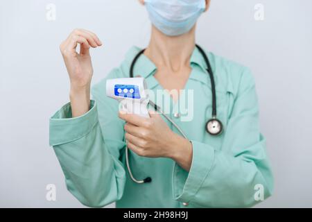Pistolet de mesure de température dans les mains du médecin.Gros plan d'un médecin portant un masque chirurgical de protection prêt à l'emploi thermomètre infrarouge isométrique Banque D'Images