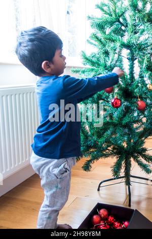 Garçon indien de 3 ans décorant l'arbre de Noël avec des boules Banque D'Images