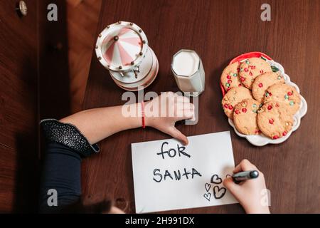 Vue de dessus d'une petite fille laissant des biscuits et un verre de lait pour le Père Noël, lui écrivant une carte Banque D'Images