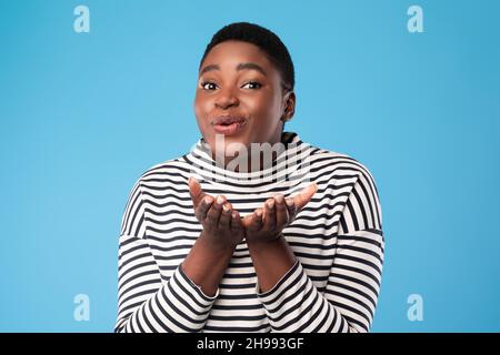 Une femme noire gaie de plus grande taille envoie des bisous d'air sur fond bleu Banque D'Images