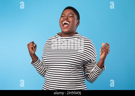 Emotive Black femme criant gesting Oui dans la joie, fond bleu Banque D'Images