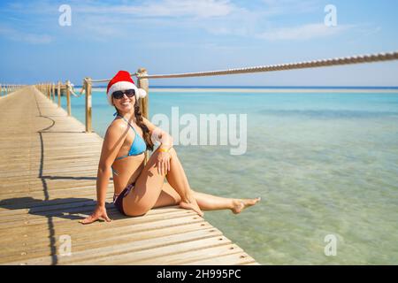bonne jeune femme au chapeau de père noël assise sur un ponton en bois Banque D'Images