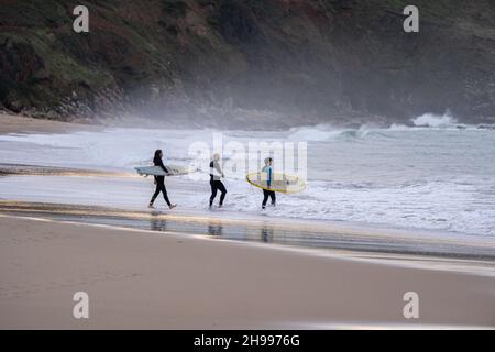 Trois surfeurs entrent dans l'eau pour faire du surf sur la plage toujours populaire de PRAA Sands sur la côte sud de Cornwall. Banque D'Images