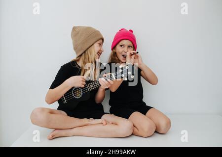 Petits frères et sœurs jouant avec des instruments de musique, ayant du plaisir, faisant semblant.Ils craignent les chapeaux tricotés colorés. Banque D'Images