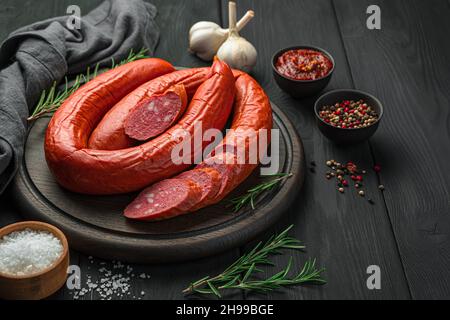 Saucisse fumée sur une planche à découper avec morceaux de tranches, romarin et épices sur fond sombre.Vue latérale, espace de copie.Antipasti. Banque D'Images