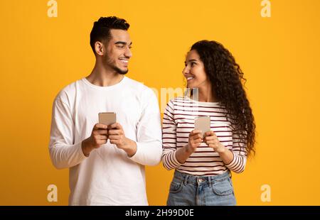 Joyeux arabe homme et femme tenant un smartphone et regardant l'un l'autre Banque D'Images