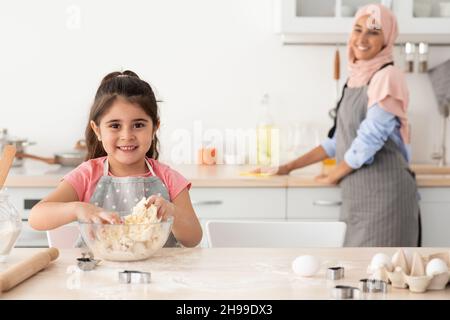 Mignonne femme enfant préparant la pâte tout en cuisant avec le maman musulmane dans la cuisine Banque D'Images