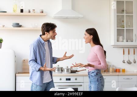 En colère offensa jeune femme et son mari cria, jure dans la cuisine intérieure.Couple arguant et conflictuel Banque D'Images