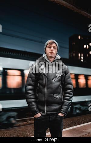 Un portrait d'un jeune homme britannique adulte portant un manteau noir avec un bonnet à la gare Banque D'Images