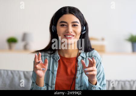 Vue en portrait d'une femme arabe gaie casque passer un appel vidéo, en utilisant l'ordinateur de la maison Banque D'Images