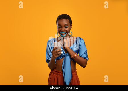 Femme noire émotive avec une tenue lumineuse à l'aide d'un smartphone Banque D'Images