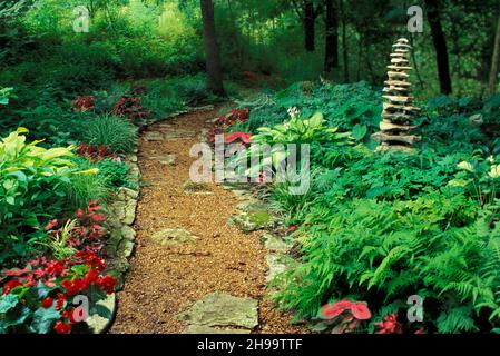 Magnifique cairn de roche fait à la main se dresse dans un jardin luxuriant ombragé avec une passerelle en gravier à travers des fougères et des fleurs florales, Missouri, Etats-Unis Banque D'Images