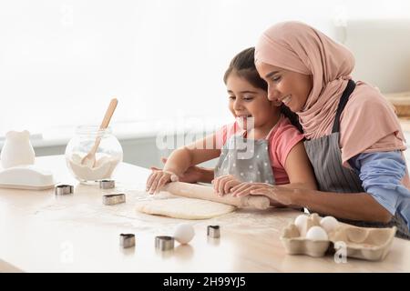 Maman musulmane attentionnée apprendre à sa petite fille comment faire rouler la pâte Banque D'Images