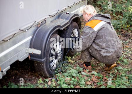 Un mécanicien de voiture gonfle les roues d'une remorque de voiture à deux essieux avec un compresseur d'air électrique portatif.Entretien et réparation des pneus. Banque D'Images